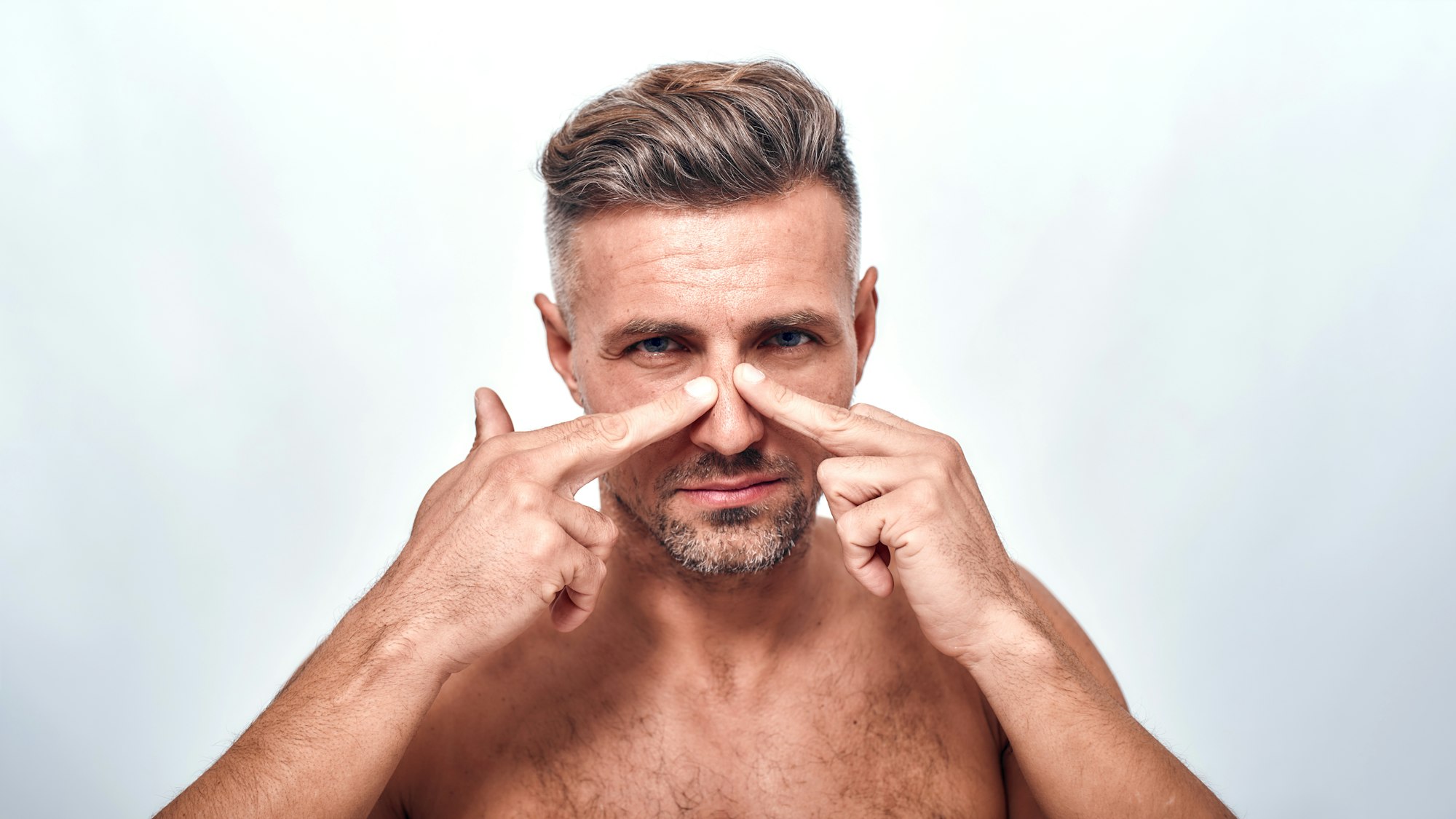 Everything should be perfect. Worried man with a stubble examining his nose and looking at camera